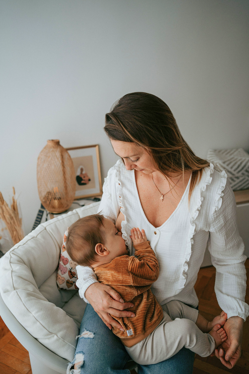 Une maman qui allaite son bébé à l'aide de la sublime blouse d'allaitement blanche aux boutons dorés
